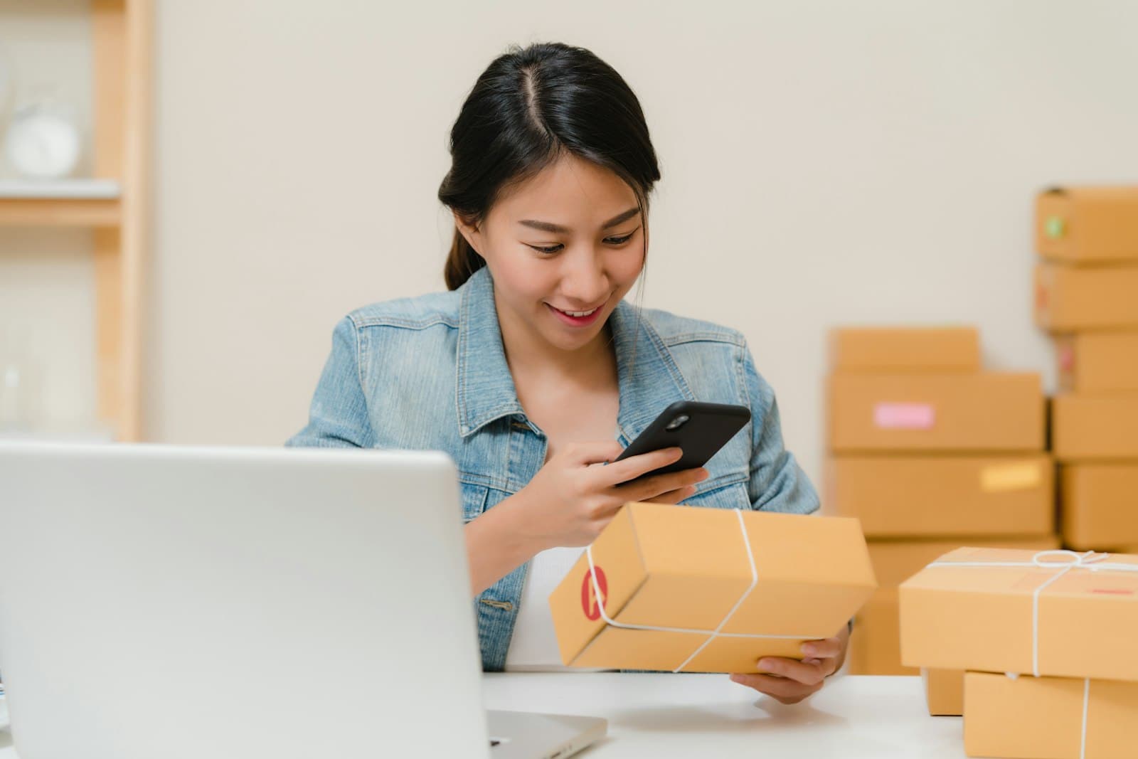 An online seller checking an order on a phone while holding a packed box